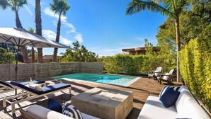 Zona junto a la piscina con sillones reclinables, un muelle de madera y un pozo de fuego de hormigón.
