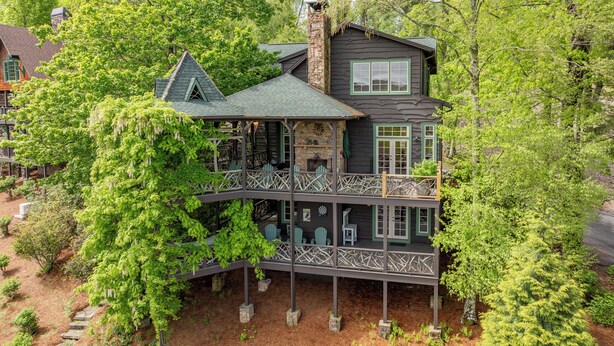 A multi-story house with a balcony, surrounded by lush greenery.