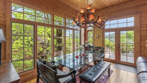 A wooden interior with large windows, a glass dining table, and a bench.