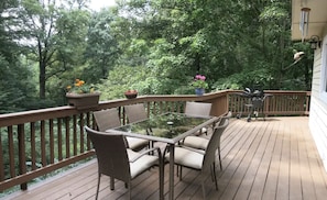 Una terraza con una mesa de vidrio y sillas de mimbre, rodeada de plantas en macetas y una barandilla de madera.