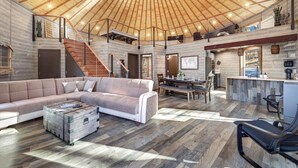 Ein geräumiger Wohnbereich mit einer großen Couch, einem Couchtisch und einem Esstisch. Eine Treppe führt zu einer oberen Ebene.