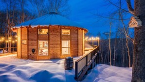 Eine Holzhütte mit verschneitem Dach, großen Fenstern und einer Terrasse mit Lichterketten.