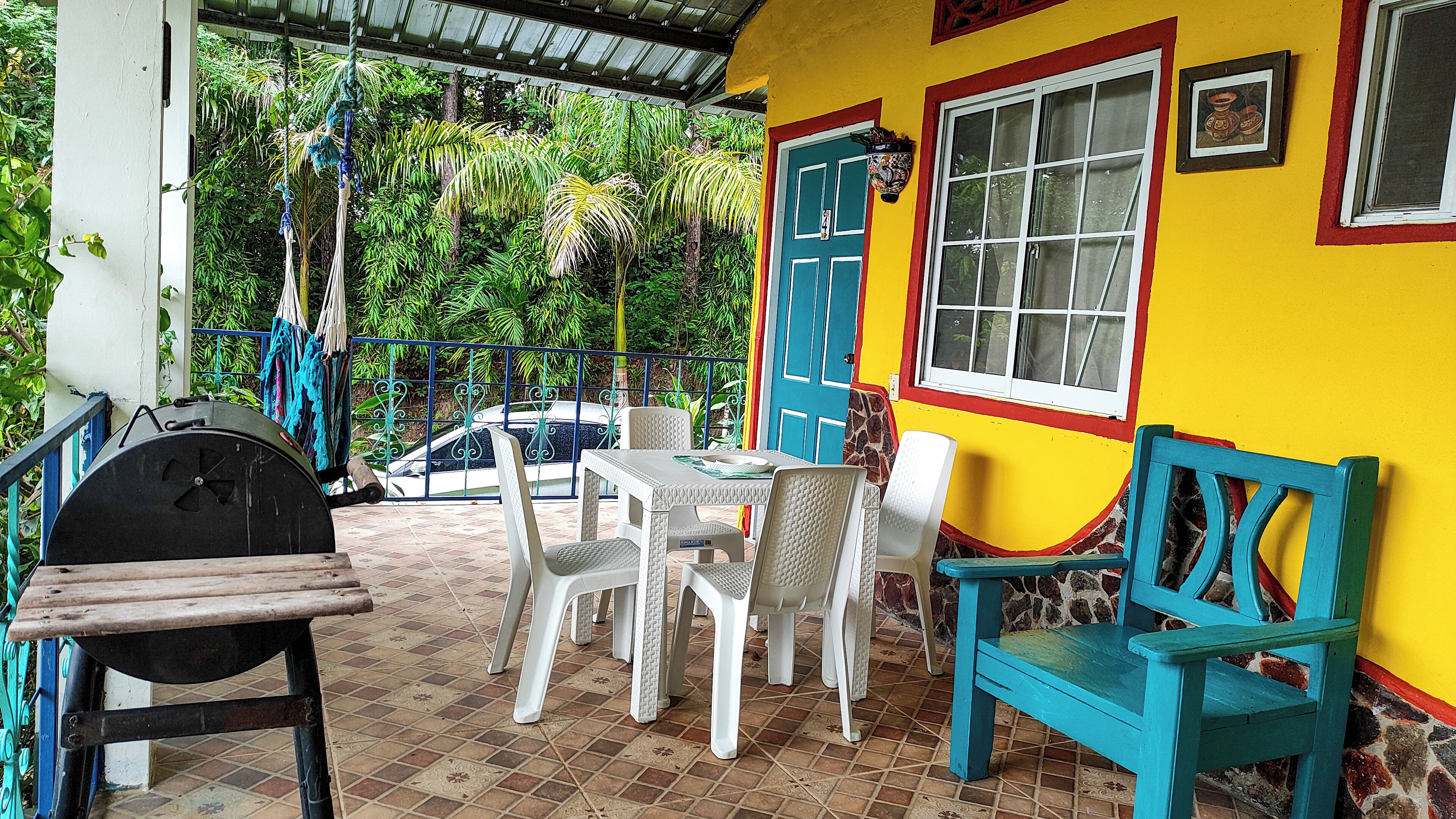 Un patio con mesa y sillas, una parrilla y un muro colorido que tiene una puerta y una ventana.