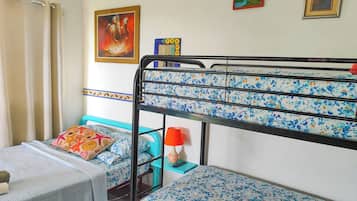 A bunk bed with a floral-patterned mattress, a small table with a white cloth, and a red lamp on a blue nightstand.