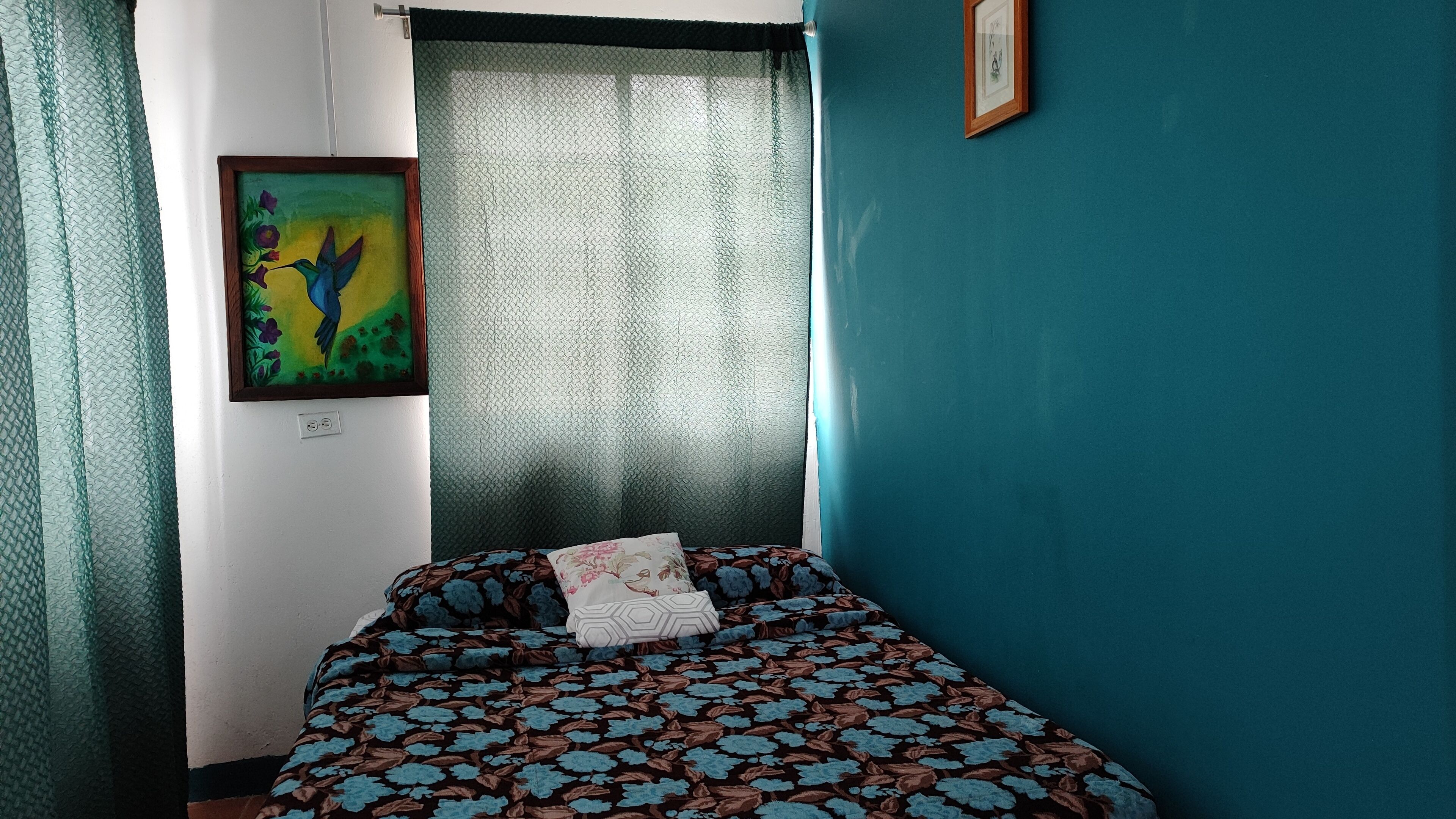 A bedroom with a bed, a painting, and a window with curtains.