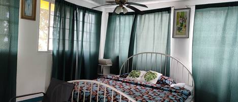 A bedroom with a bed, a chair, a ceiling fan, and curtains.