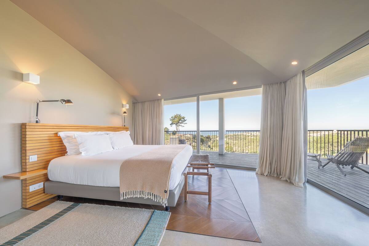 Un dormitorio moderno con una cama grande, una mesita de noche, un escritorio y un balcón con vistas.