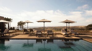 Un espace piscine doté de chaises longues et de parasols, offrant une vue sur un paysage magnifique.