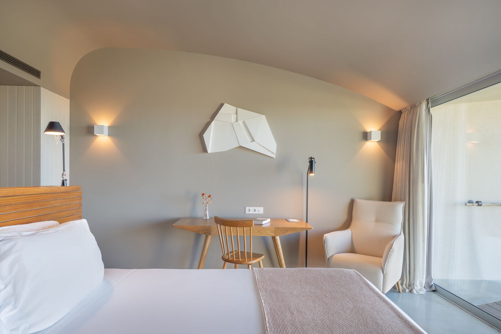 Una habitación de hotel moderna con cama, escritorio, silla y un amplio ventanal.