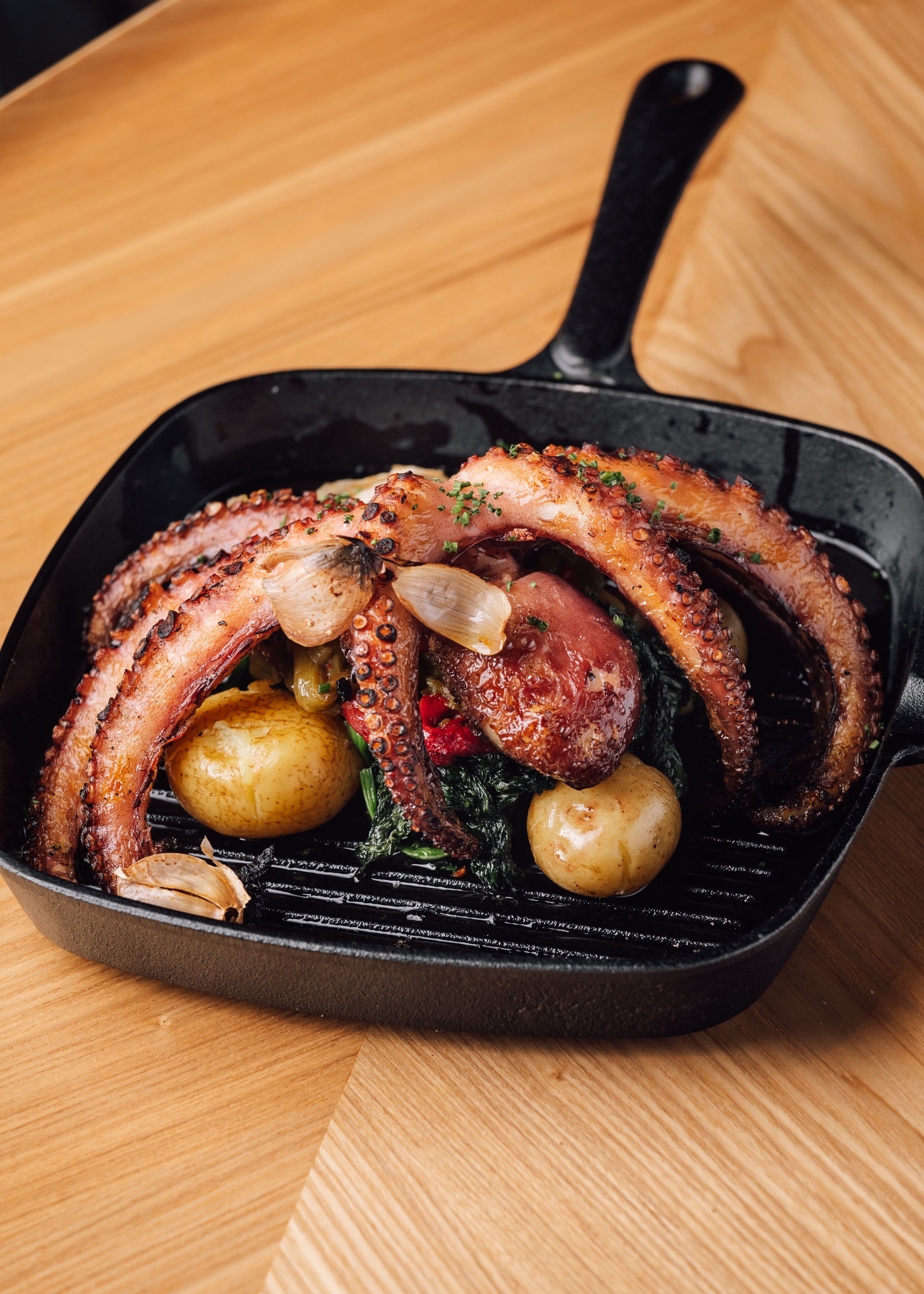 Una sartén con pulpo a la parrilla, patatas y verduras de hoja verde.