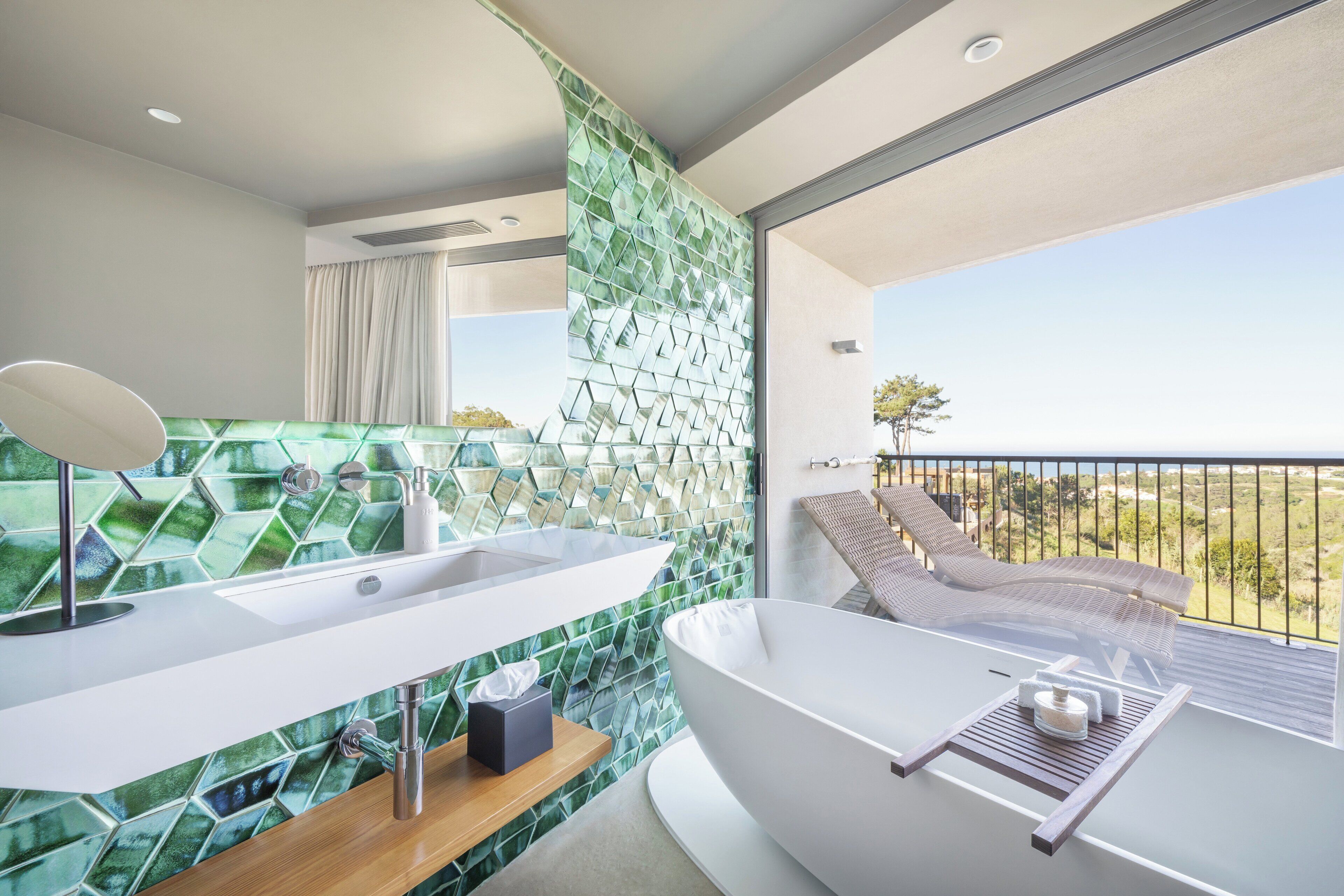 A modern bathroom with a large bathtub, a white sink, and a green mosaic wall.