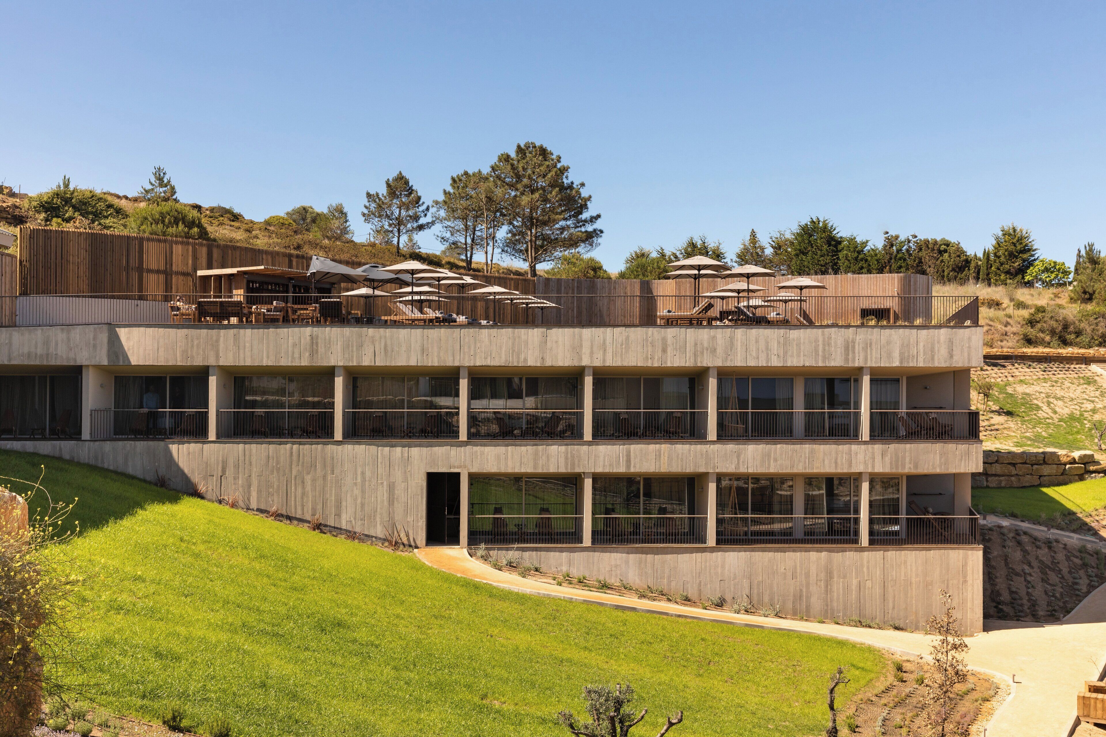 Un edificio moderno con varios balcones, mobiliario exterior y un césped bien cuidado.
