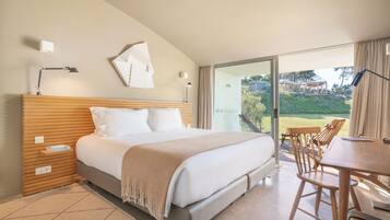 Quarto com uma cama grande, cabeceira de madeira, escrivaninha com cadeiras e vista para o exterior.