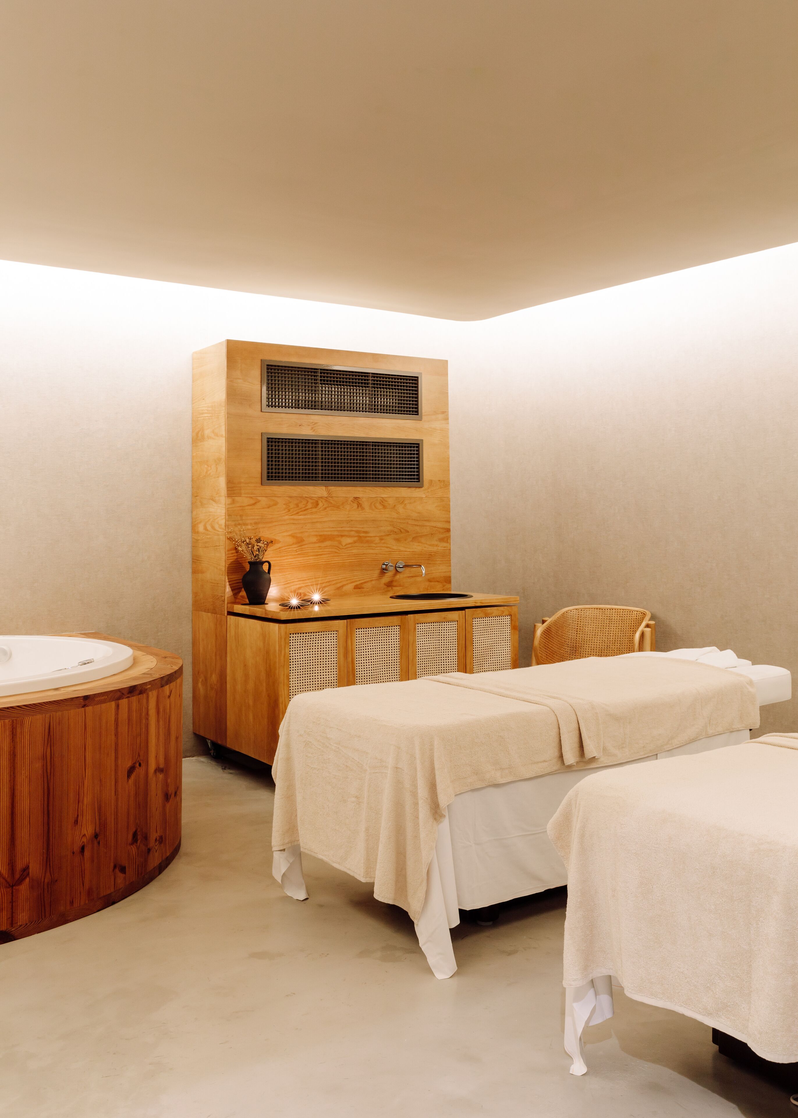 Un moderno cuarto de spa con un mueble de madera, una bañera redonda y dos camillas de tratamiento.