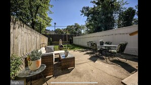 A patio area with outdoor furniture, including wicker chairs and a table, surrounded by a wooden fence and trees. - Home Sweet Home @Trolley Square!<br><br>https://goo.gl/maps/f1XX68qiTRCU7eFk7<br> (Wilmington)