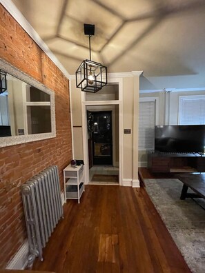 A modern living room with a brick wall, a large TV, and a wooden floor. - Home Sweet Home @Trolley Square!<br><br>https://goo.gl/maps/f1XX68qiTRCU7eFk7<br> (Wilmington)