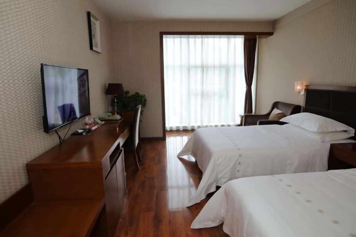 A hotel room with two beds, a desk with a TV, a chair, and a window with curtains.