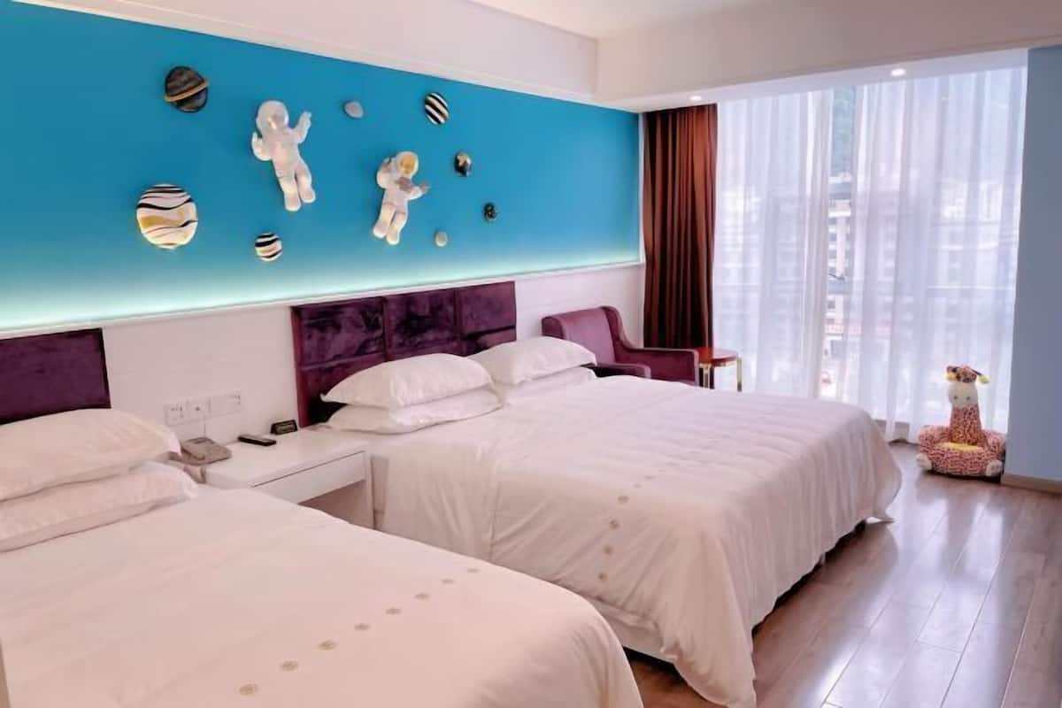 A hotel room with two beds, a blue accent wall, and a city view.