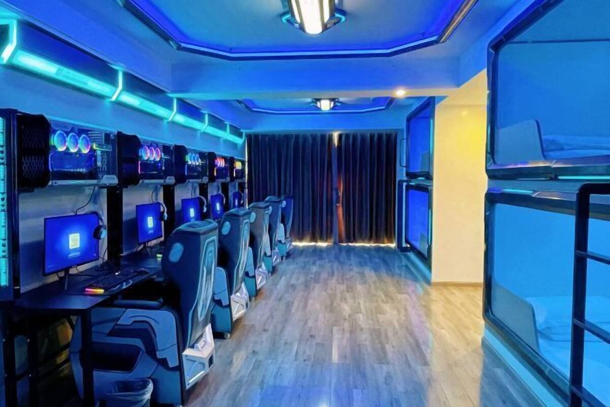 A row of gaming PCs with monitors, chairs, and a wooden floor in a room with blue lighting.