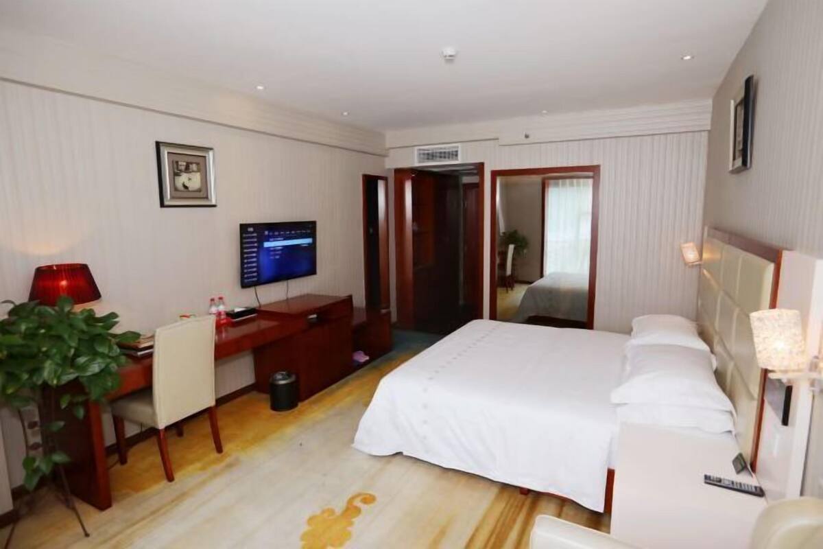 A hotel room with a bed, desk, television, and a plant.