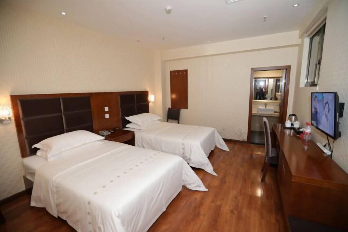 A hotel room with two beds, a wooden floor, a desk with a TV, and a mirror.