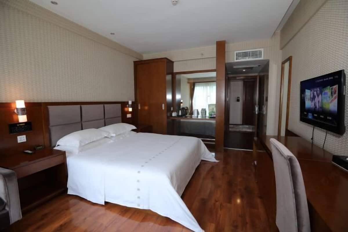 A hotel room with a large bed, a desk, a television, and a bathroom visible through an open door.