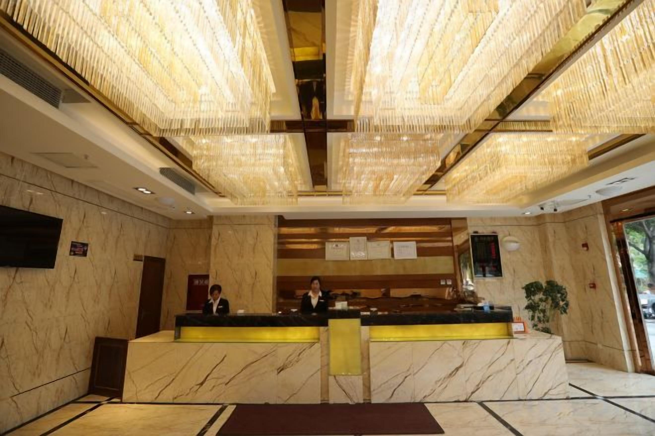 Een hotel receptie met een marmeren balie, een grote kroonluchter en een flatscreen televisie aan de wand.