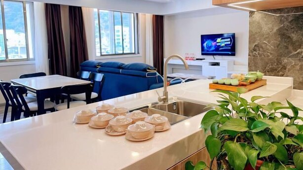 A modern hotel room with a dining area, a large window, a television, and a sink with tea sets. - Tonghe Hotel (Shimian)