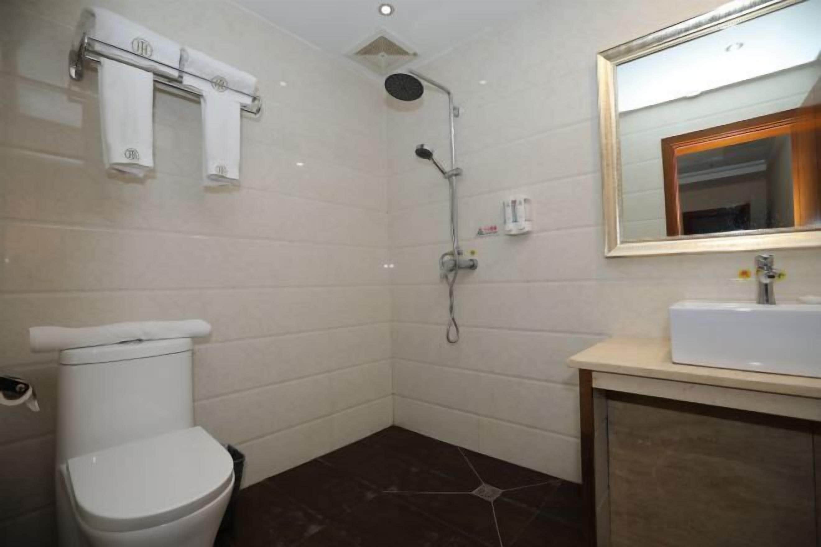 A bathroom with a toilet, a shower, a sink, and a mirror.