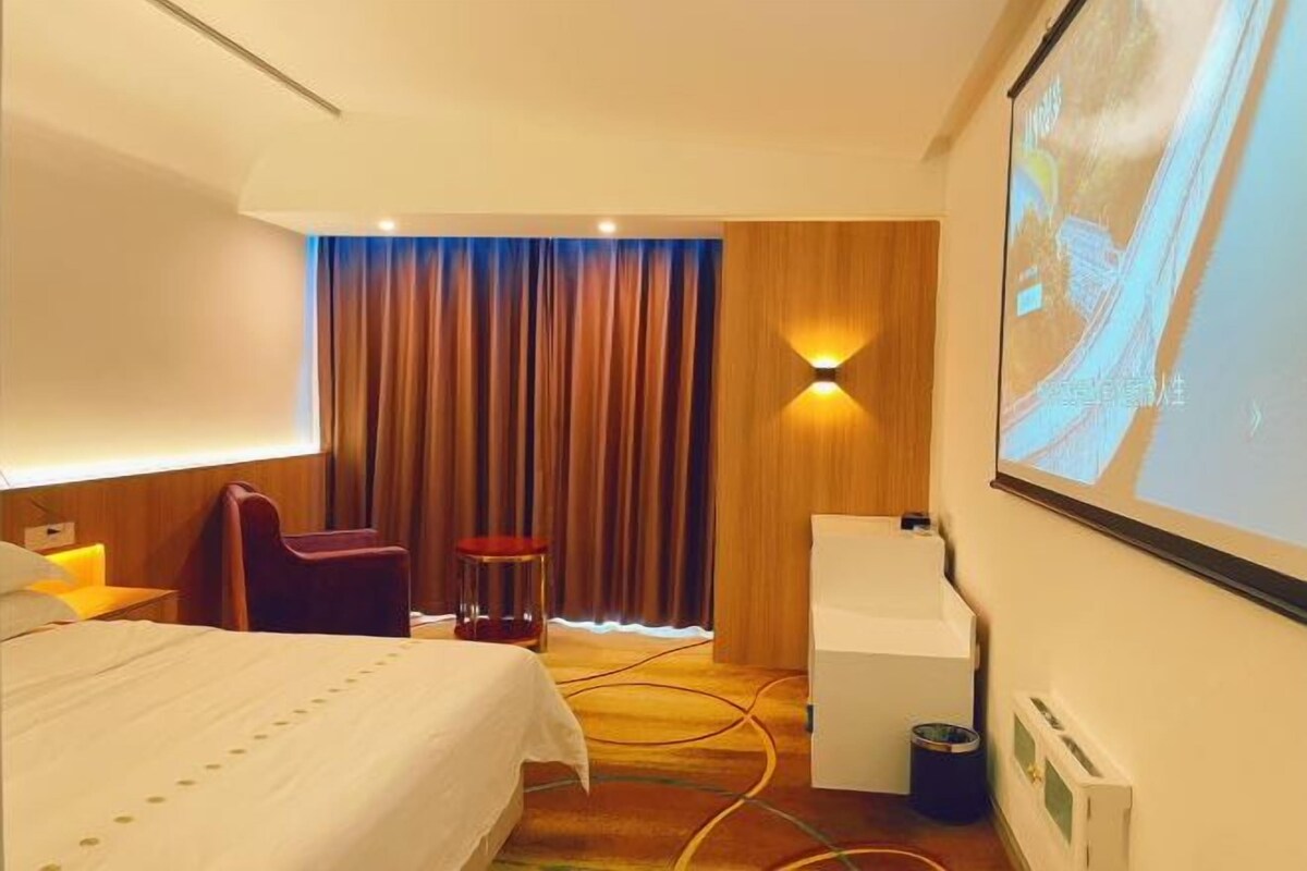 A hotel room with a bed, a desk, a chair, a projector screen, and a curtain.