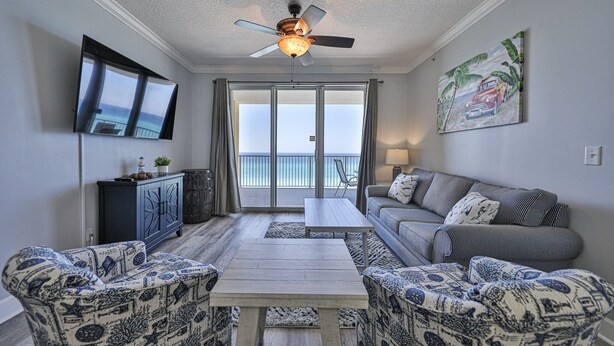 A living room with a sofa, two patterned armchairs, a coffee table, a ceiling fan, a TV, and a painting.