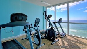 A gym with cardio machines and a treadmill, large windows with a view of the ocean.