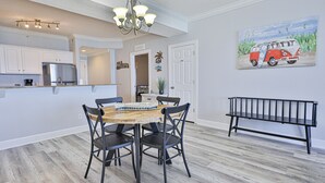 A dining area with a wooden table and black chairs, a kitchen with white cabinets and stainless steel appliances, and a bench against the wall.