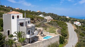 A modern two-story house with a stone retaining wall, a swimming pool, and a view of the coastline. - Villaki studio geust house,Private pool (Maroulas)