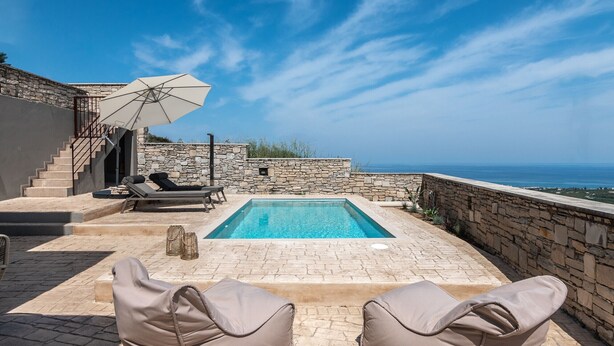 A rooftop pool area with stone walls, a pool, lounge chairs, and a view of the sea. - Villaki studio geust house,Private pool (Maroulas)