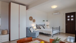 A bedroom with a bed, a blue armchair, a dining table with fruit, a wardrobe, and a small shelf with plants. - Villaki studio geust house,Private pool (Maroulas)