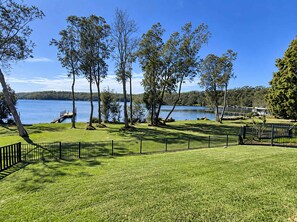 A grassy area with a lake and trees, a dock, and a fenced section.