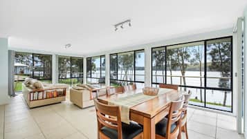 Enjoy meals at the large dining table surrounded by comfortable chairs, with a view of the lake and trees.