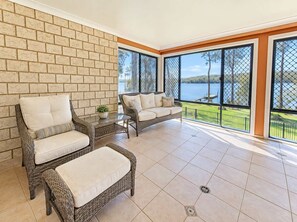 A sunlit room with wicker furniture, a brick wall, and a view of a lake.