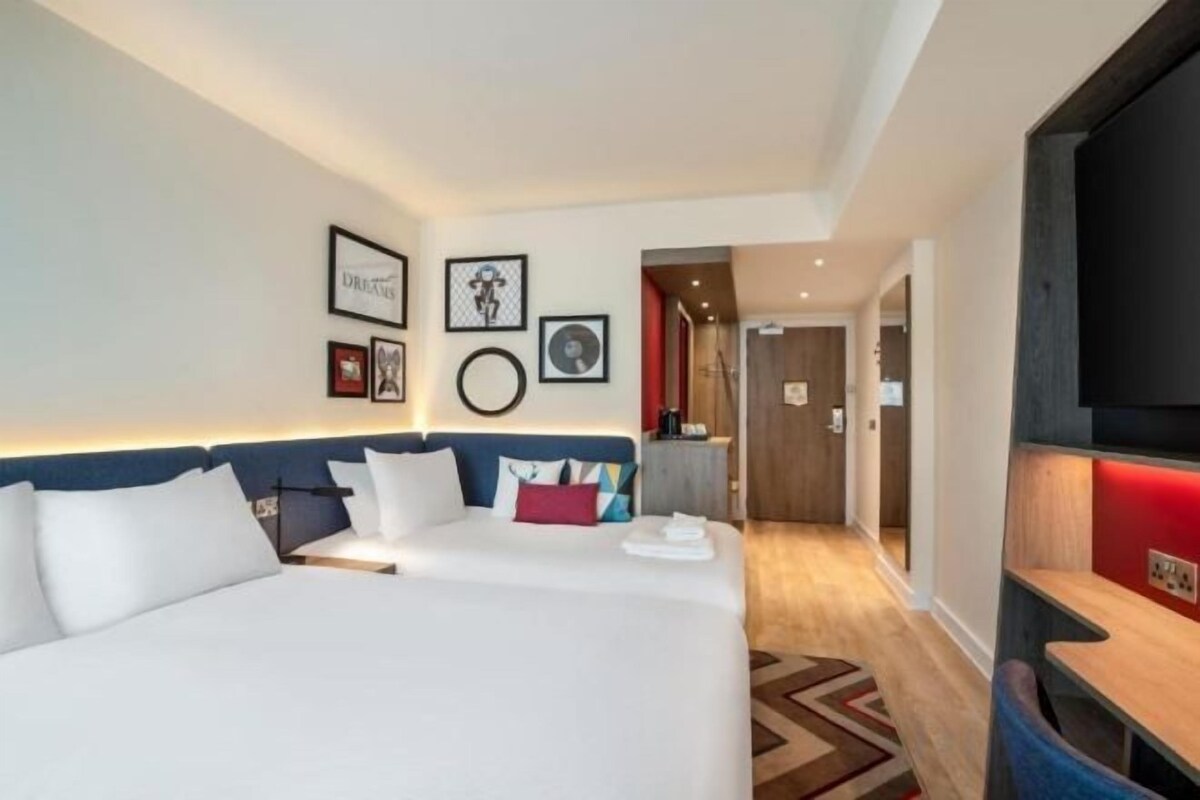Une chambre d’hôtel avec un grand lit, un bureau, une télévision et une porte donnant sur un couloir.
