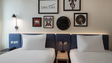 A hotel room with a bed, a nightstand, a lamp, and wall art including framed pictures and a vinyl record.