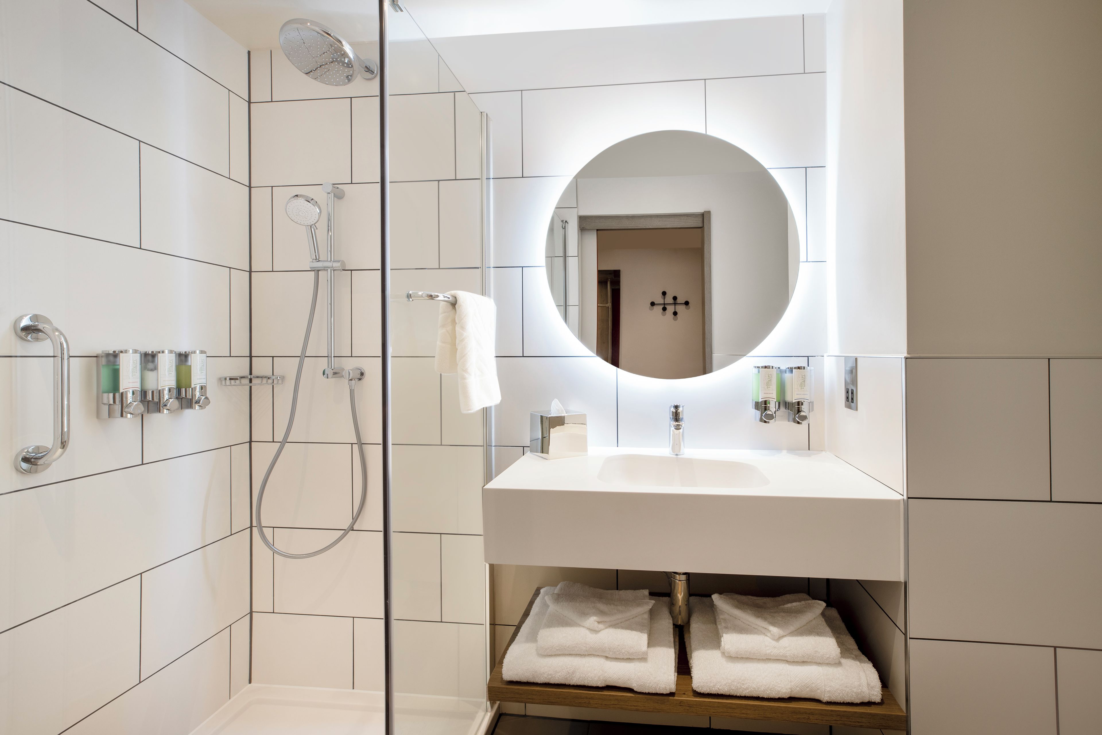 Een moderne badkamer met een douchecabine van glas, een wastafel met spiegel en netjes opgevouwen handdoeken op een plank.