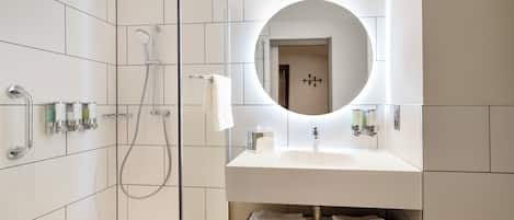 Een moderne badkamer met een douchecabine van glas, een wastafel met spiegel en netjes opgevouwen handdoeken op een plank.