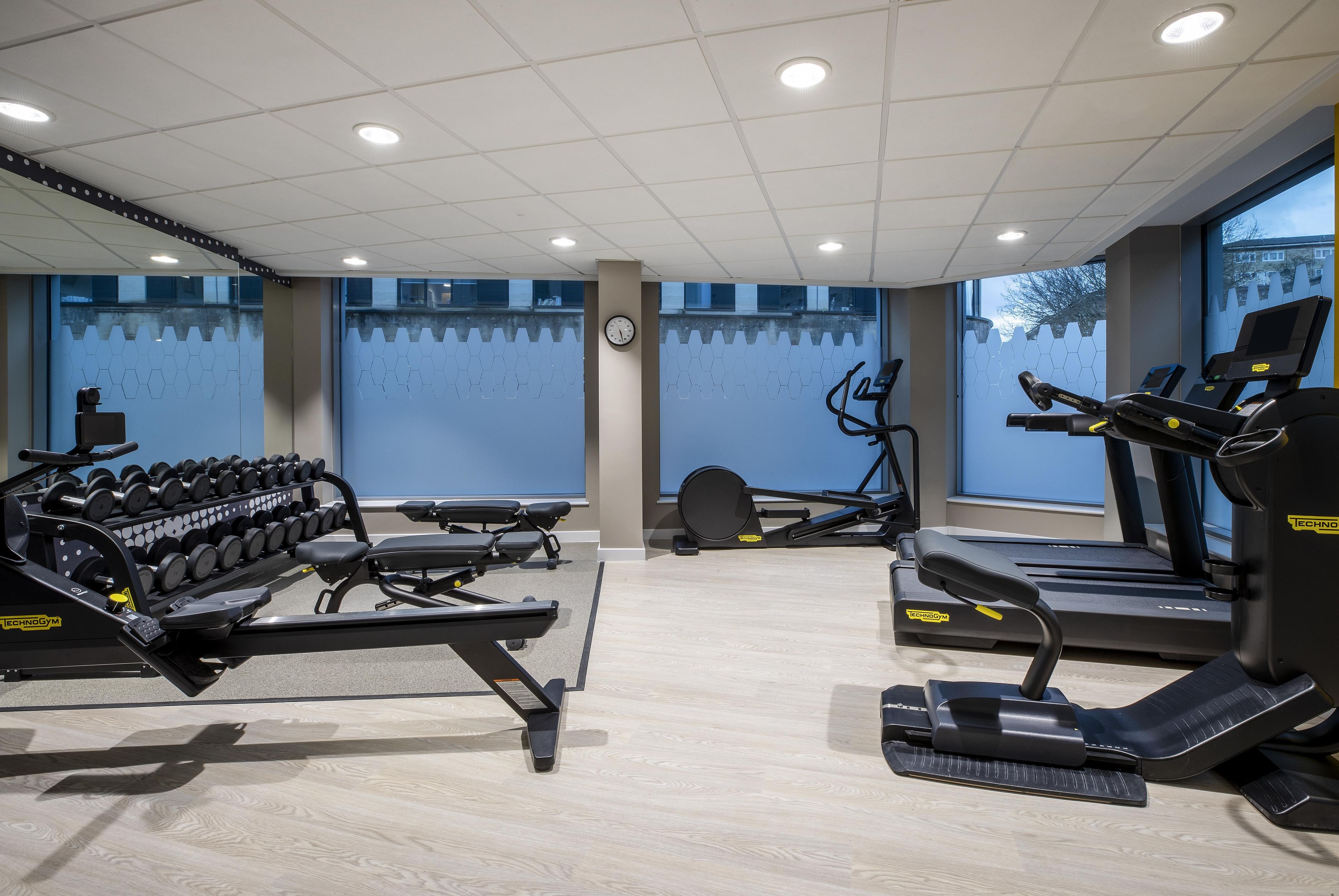 A gym with exercise equipment, a clock, and a window with a view.