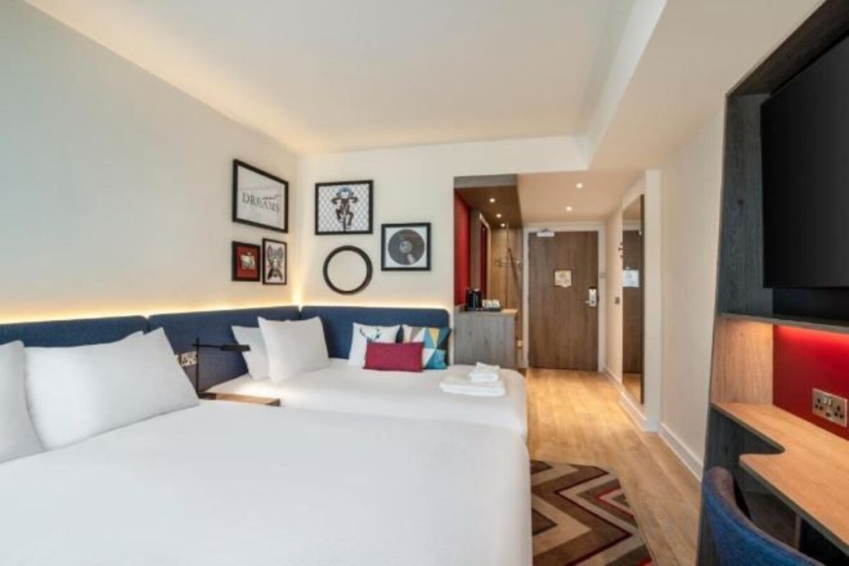 Habitación de hotel con una cama grande, un escritorio, un televisor y una puerta que da a un pasillo.