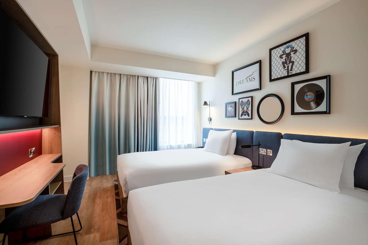 Una habitación de hotel con dos camas, un escritorio, un televisor y una ventana con cortinas.