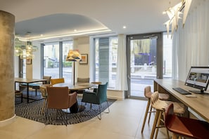 Un moderno vestíbulo de hotel con área de estar, mostrador de recepción y grandes ventanales con vista a la calle.
