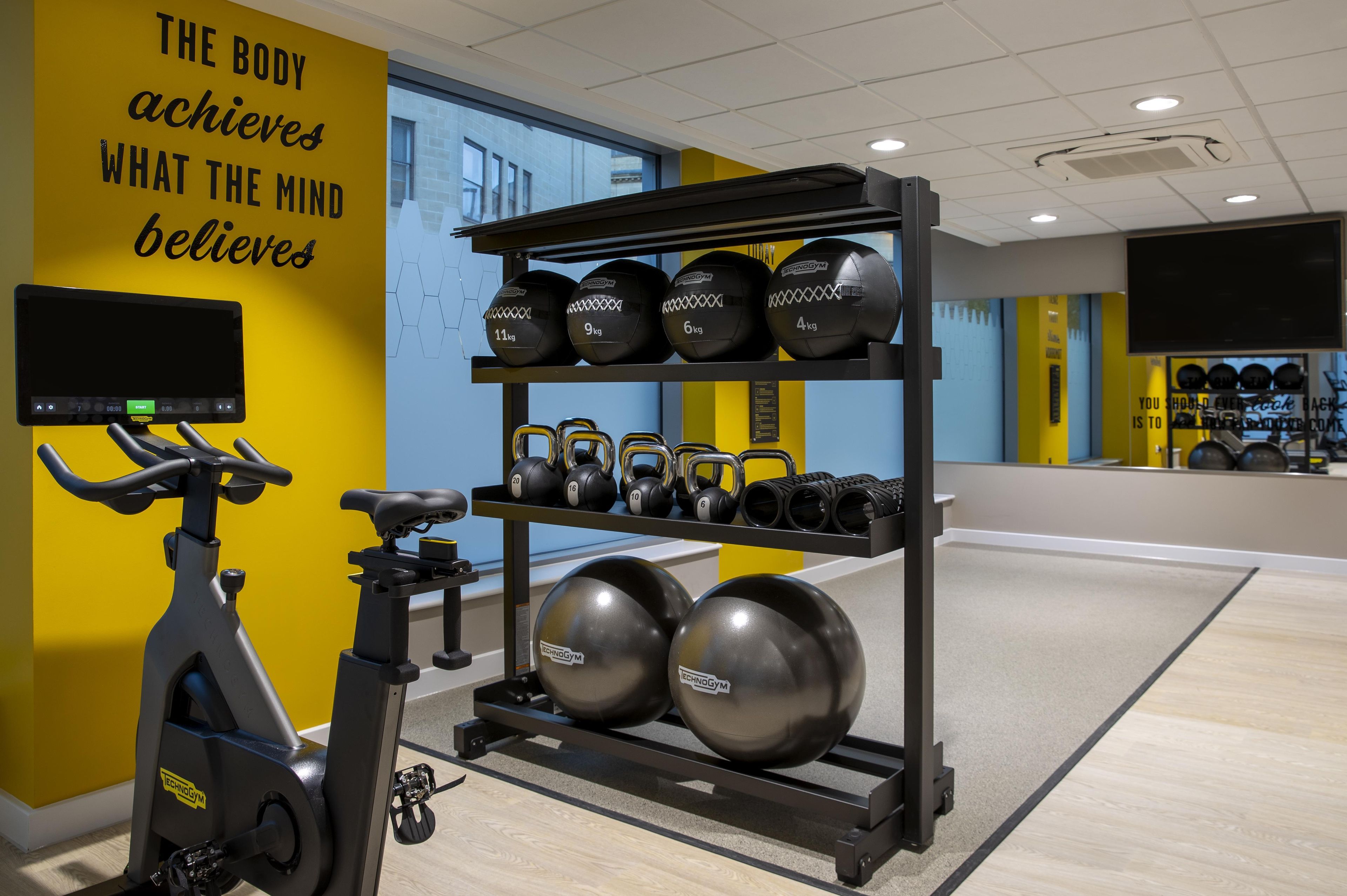 Un gimnasio con equipo de ejercicio, una bicicleta estática y una frase motivacional en la pared.
