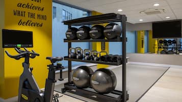 Un gimnasio con equipo de ejercicio, una bicicleta estática y una frase motivacional en la pared.