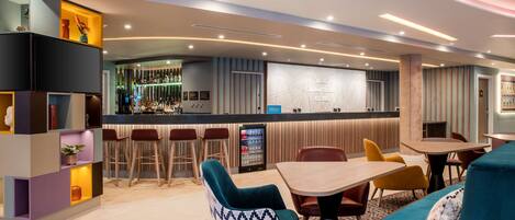 A modern hotel lobby with a bar area, seating arrangements, and a reception desk.